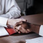 Dvije osobe se rukuju iznad ugovora na stolu